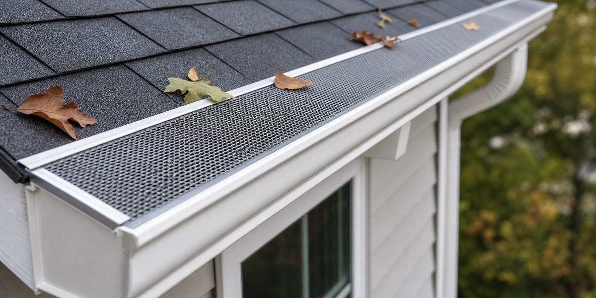 gutter guard installed over a white gutter with leaves nearby